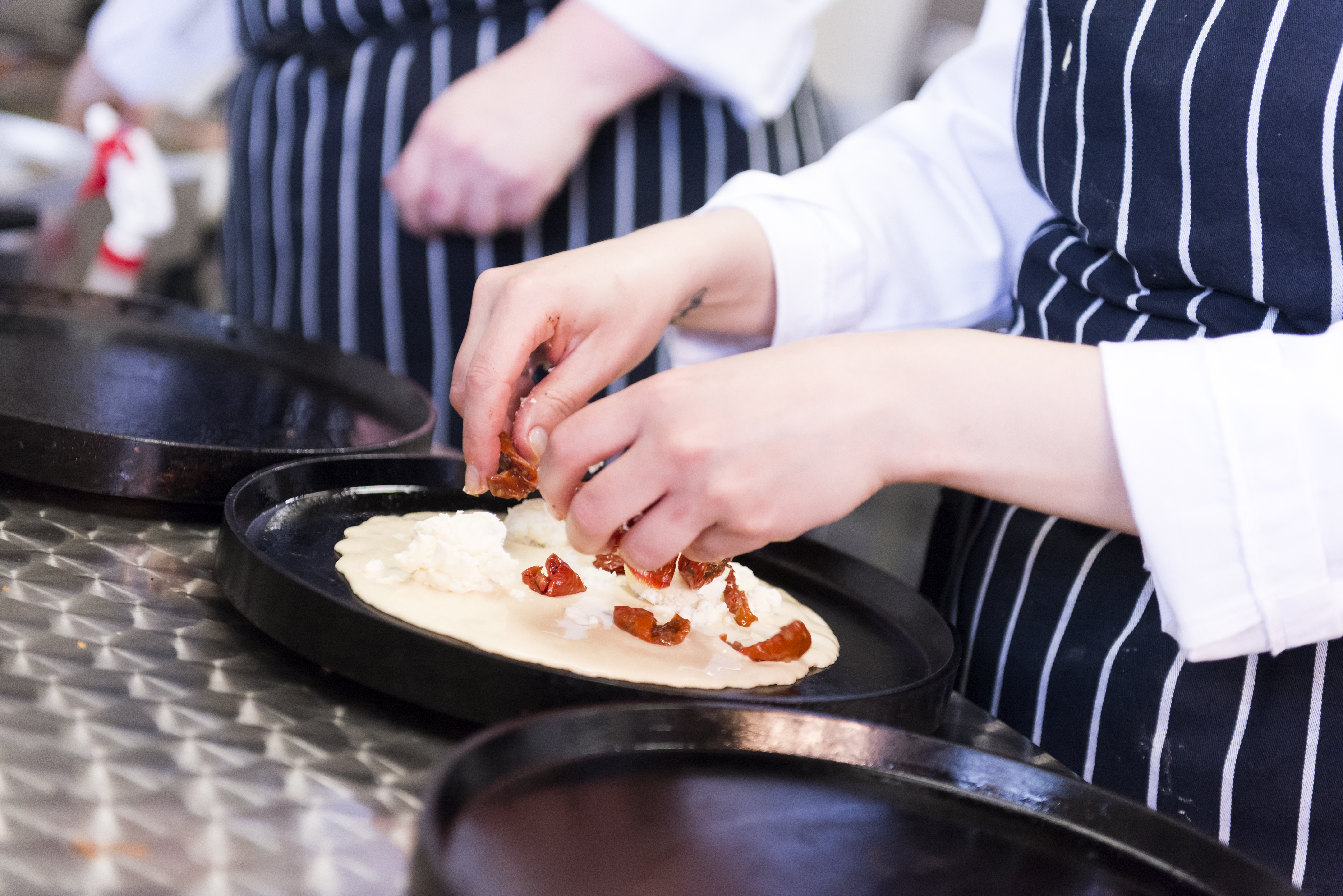 Chef adding toppings to a pancake on a griddle.