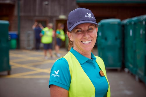 Smiling woman in work uniform, cap, and vest.
