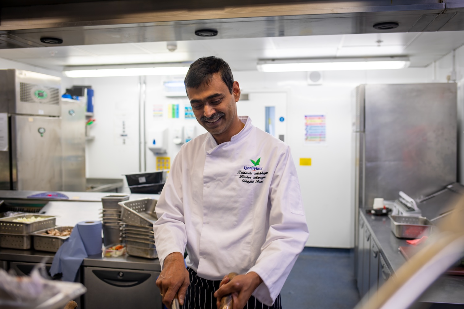 Chef in white coat smiling in a commercial kitchen.