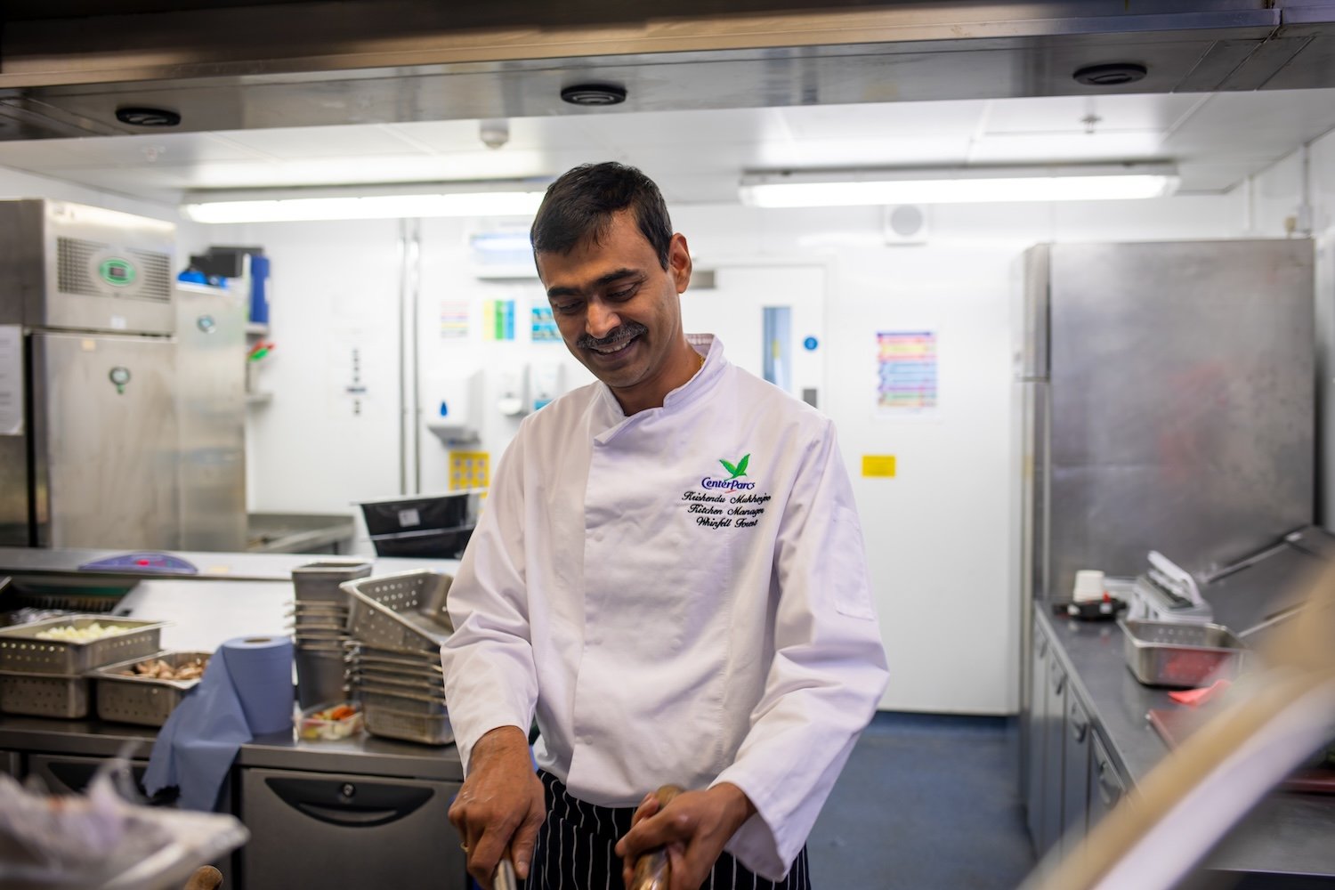 Chef in white coat smiling in a commercial kitchen.