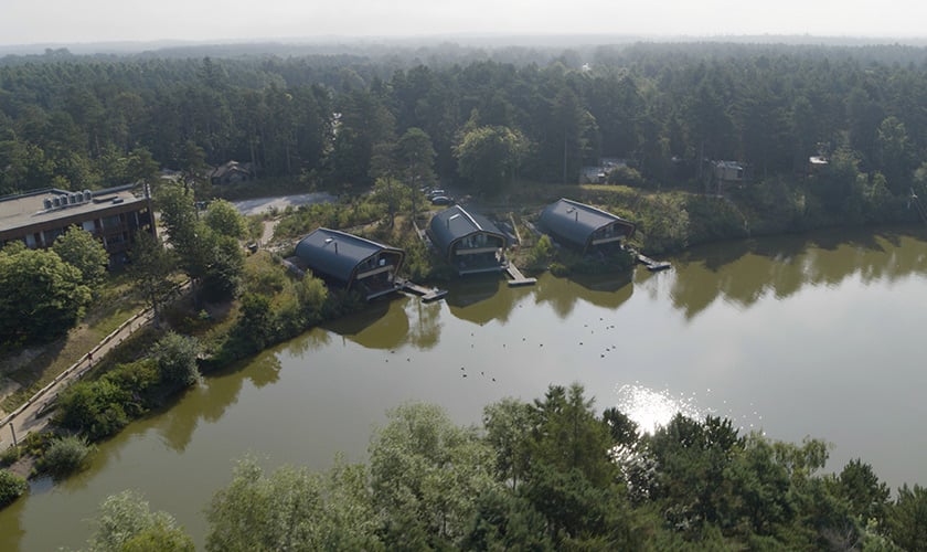 Aerial view of waterside lodges and surrounding forest.