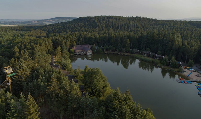 Aerial view of Whinfell Forest with lake, cabins, and trees.