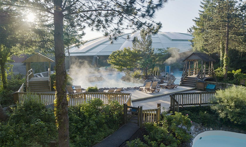 Outdoor pool with steam, wooden walkways, and trees.