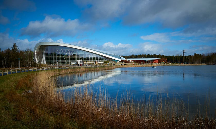 Modern building with a lake in front of it, under a cloudy sky.
