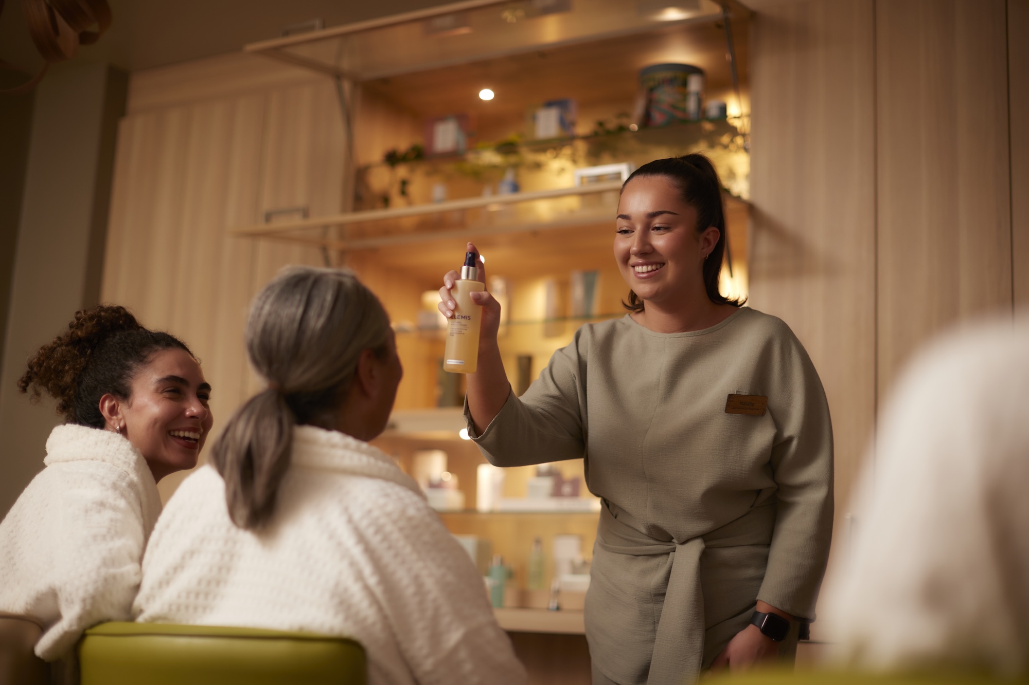 Woman spraying product, two others in robes.