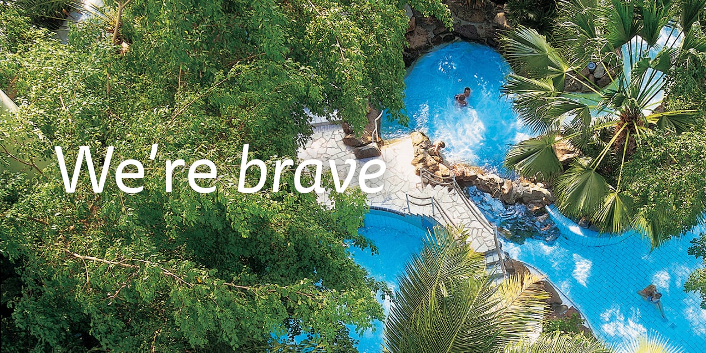 People relaxing in a pool surrounded by greenery with the text "We're brave" overlayed.