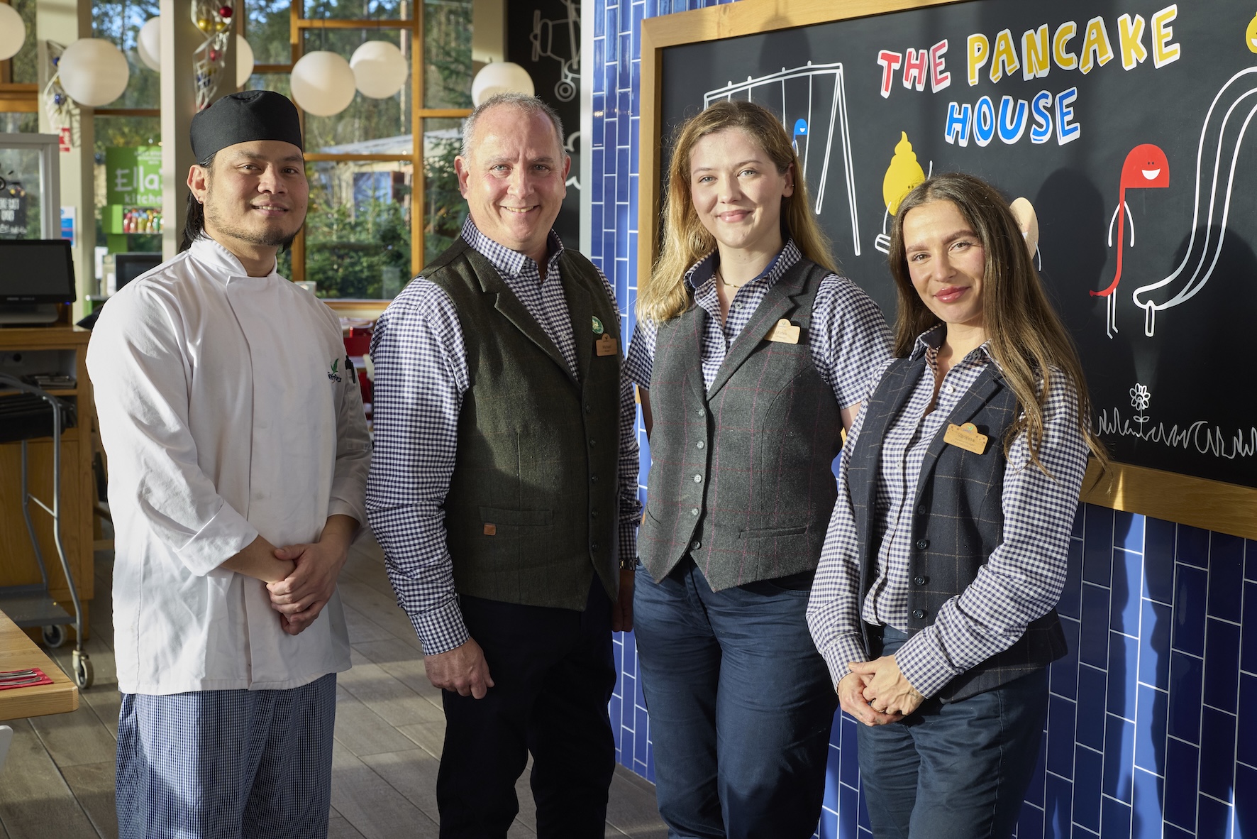 A chef and three staff members stand in front of a blackboard with "The Pancake House" written on it.