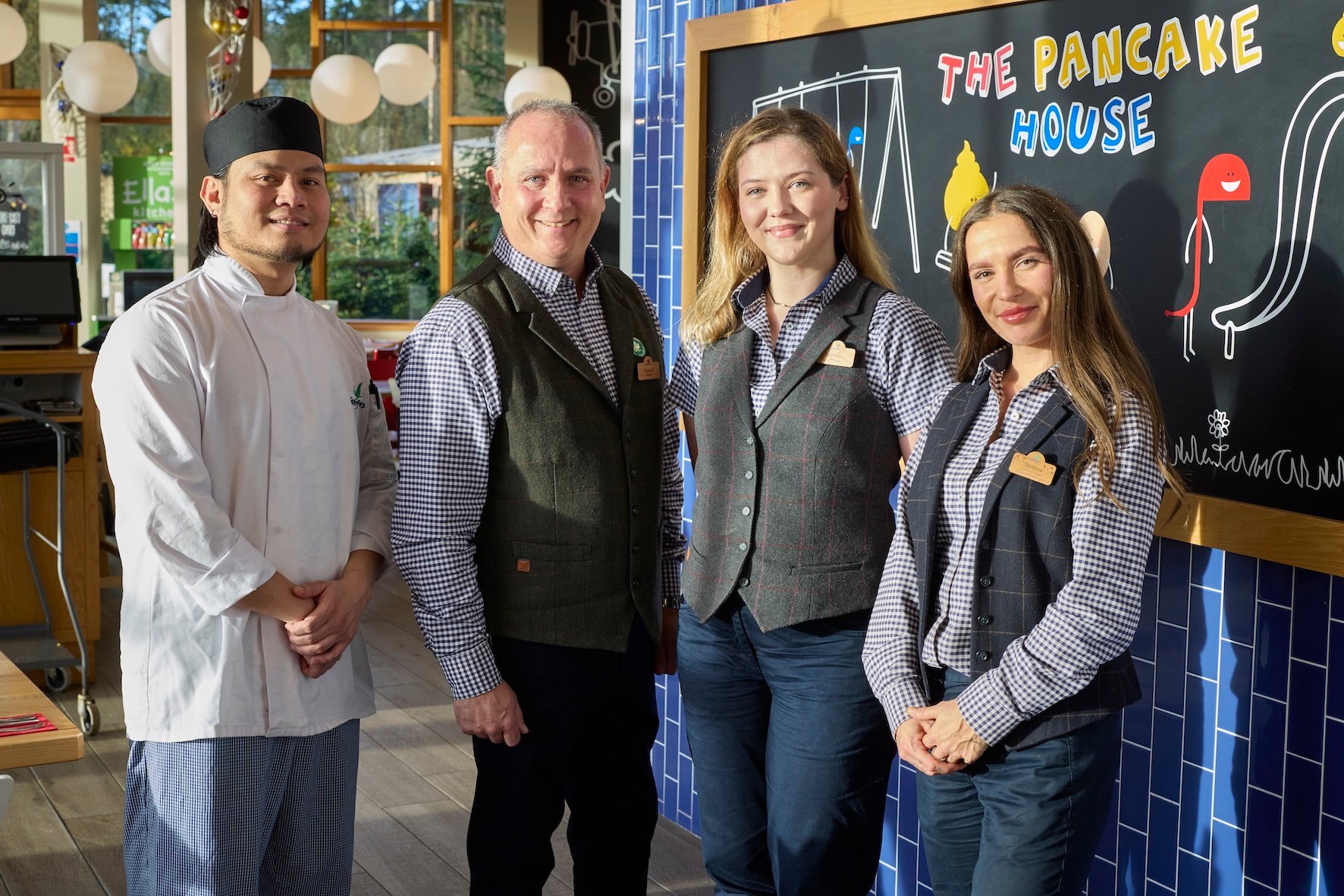 A chef and three staff members stand in front of a blackboard with "The Pancake House" written on it.